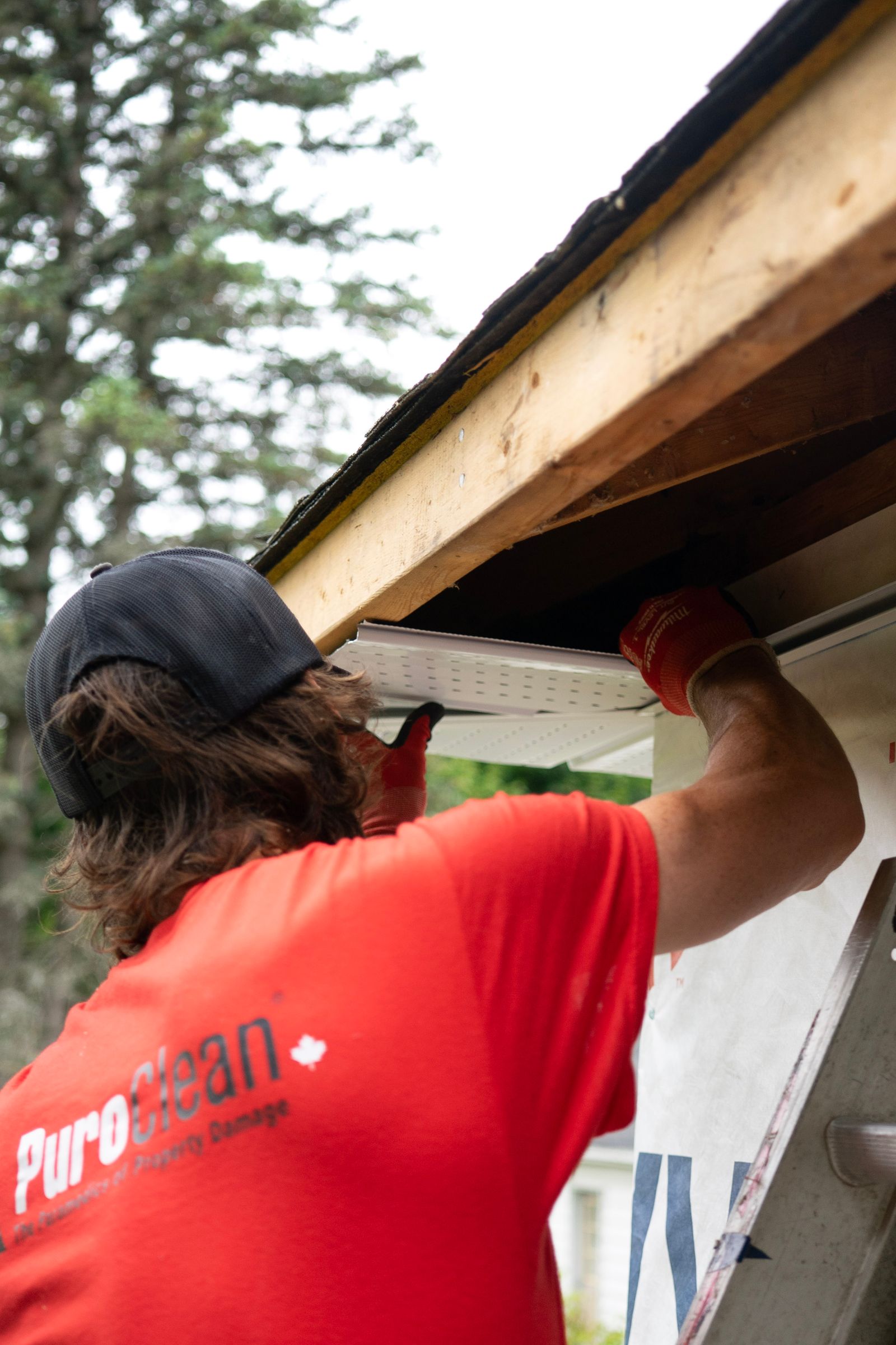 Worker clearing debris from residential gutters and checking downpipes